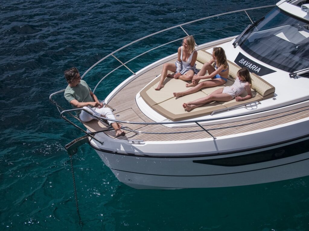 Motoryacht chartern in Neustadt in Holstein: Eine Familie entspannt auf den Sonnenpolstern am Bug der vor Anker liegenden BAVARIA SR38 bei Hanse Yachtcharter.