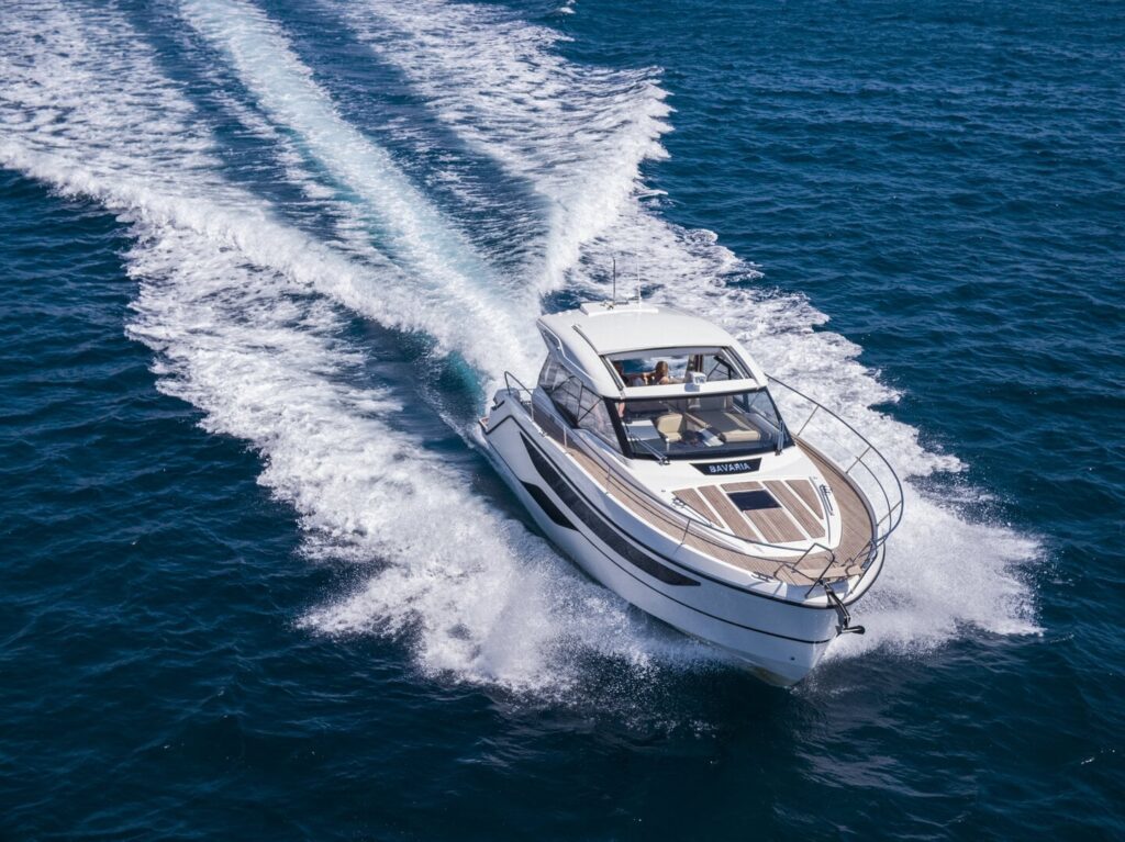 Motoryacht chartern in Neustadt in Holstein: Dynamische Luftaufnahme der BAVARIA SR38 von Hanse Yachtcharter in schneller Gleitfahrt schräg von vorne.